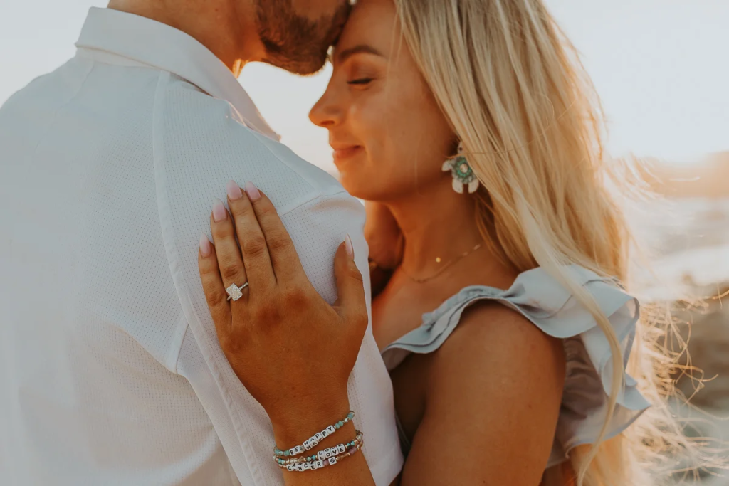 man kisses fiance on forehead, detail shot of her hand with the engagement ring