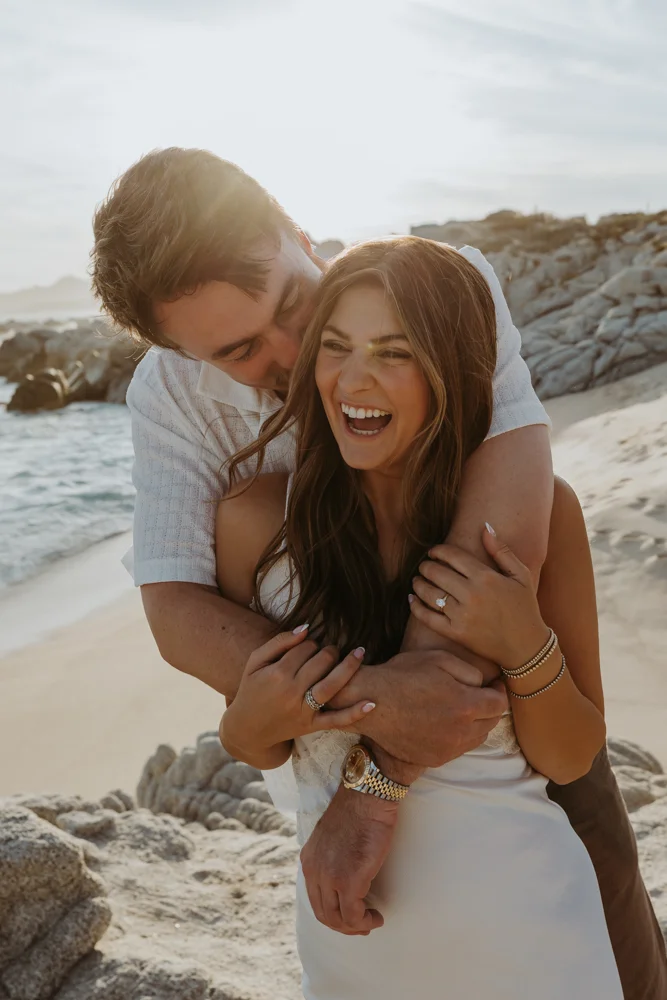 bride laughing as groom hugs her during beach photo shoot