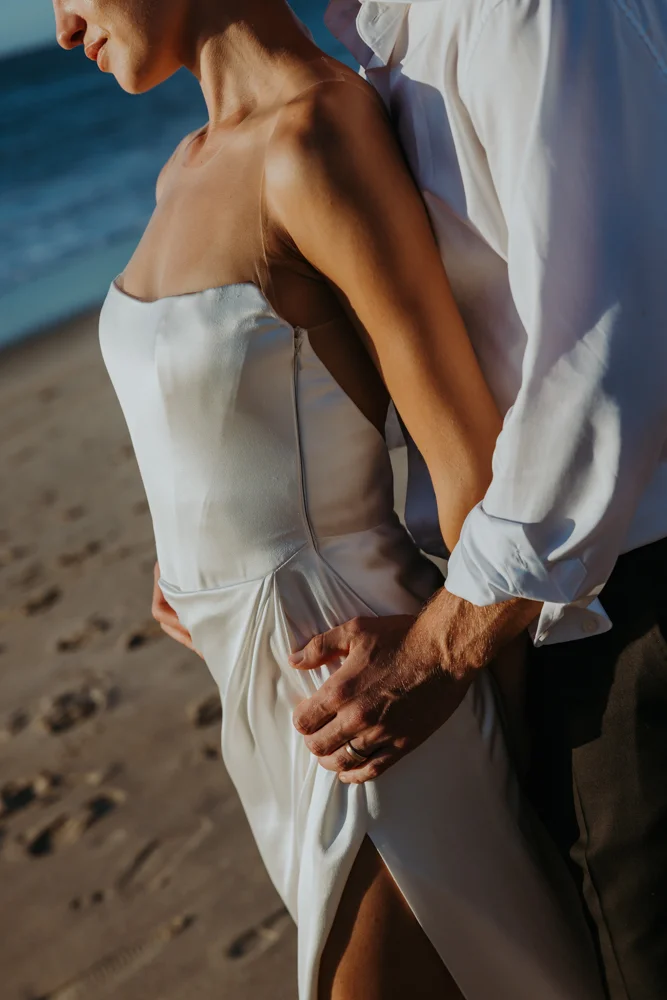 Detail photo of the arms of the groom hugging the bride with the sunlight hitting them