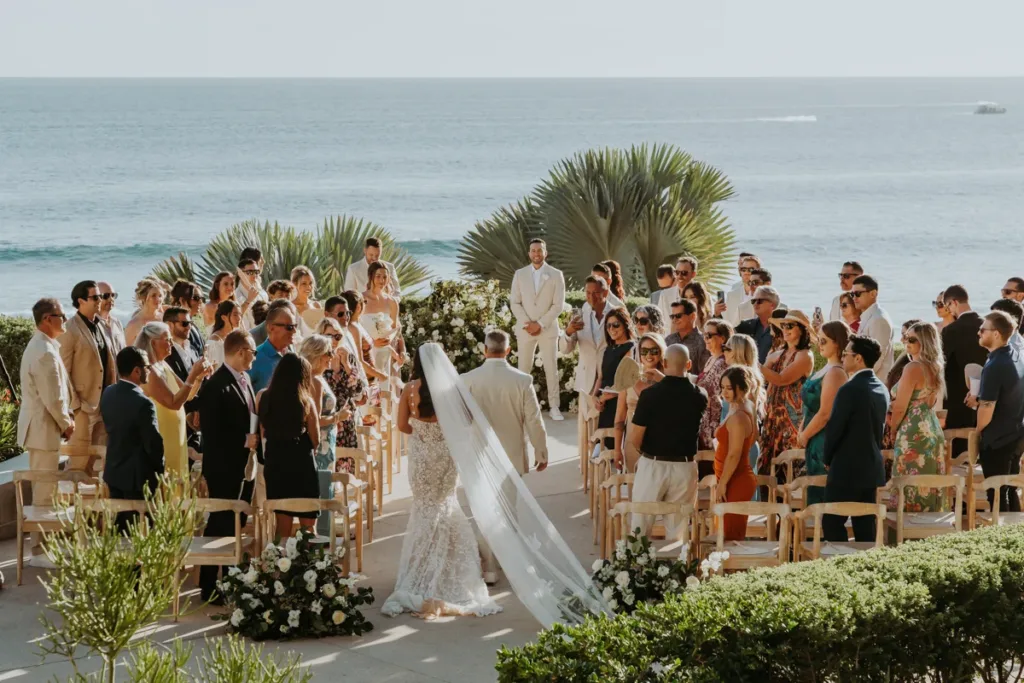 Bride walks down the aisle towards the groom, the shot is from behind and the ocean is the background