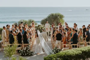 Bride walks down the aisle towards the groom, the shot is from behind and the ocean is the background
