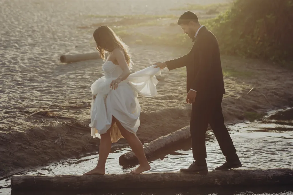 Bride and groom walk over a log to cross a river