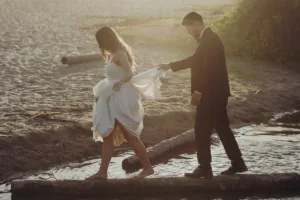 Bride and groom walk over a log to cross a river