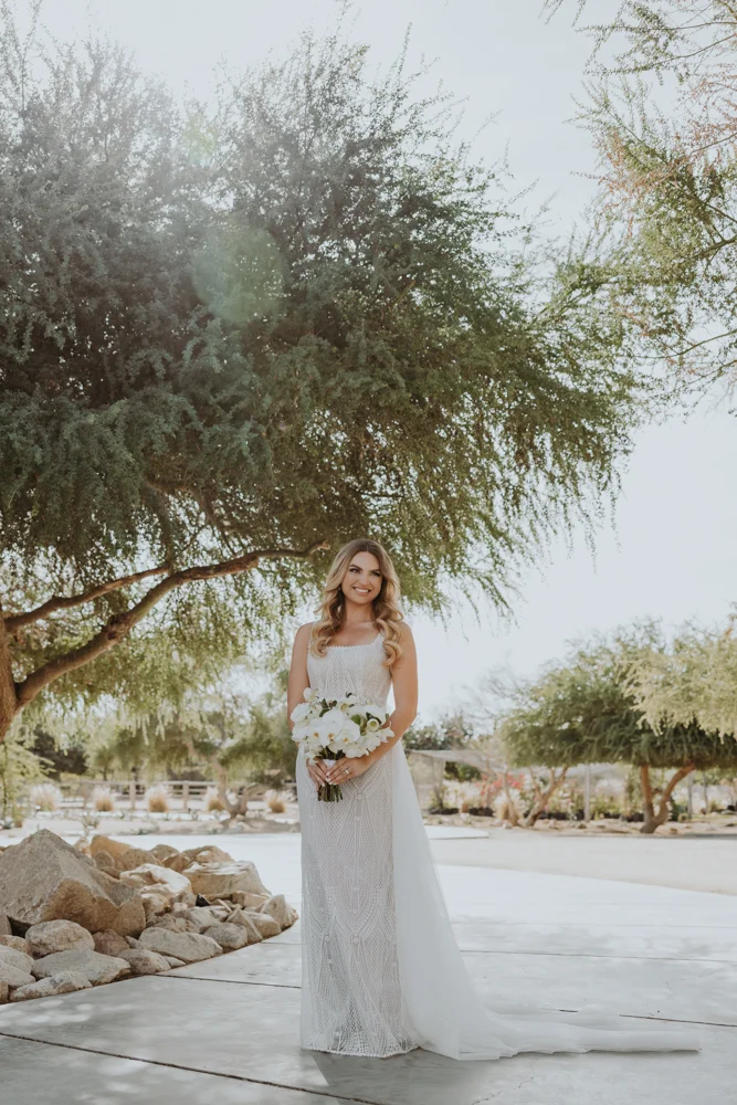 Bride smiles to the camera, she stands underneath a tree